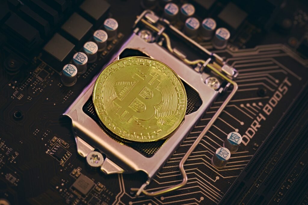 Uma moeda de Bitcoin em uma placa-mãe de computador, destacando componentes eletrônicos ao fundo.