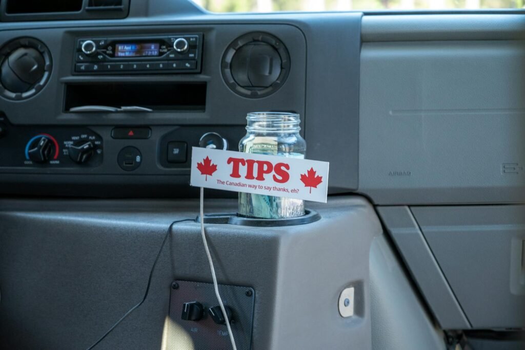 A tip jar labeled 'The Canadian way to say thanks' inside a vehicle's dashboard.