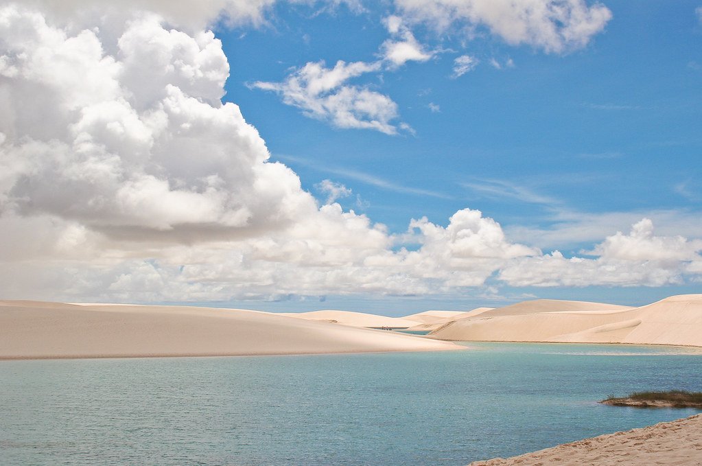 Vista panorâmica dos Lençóis Maranhenses, com dunas de areia branca e lagoas de água cristalina sob um céu azul e nublado.