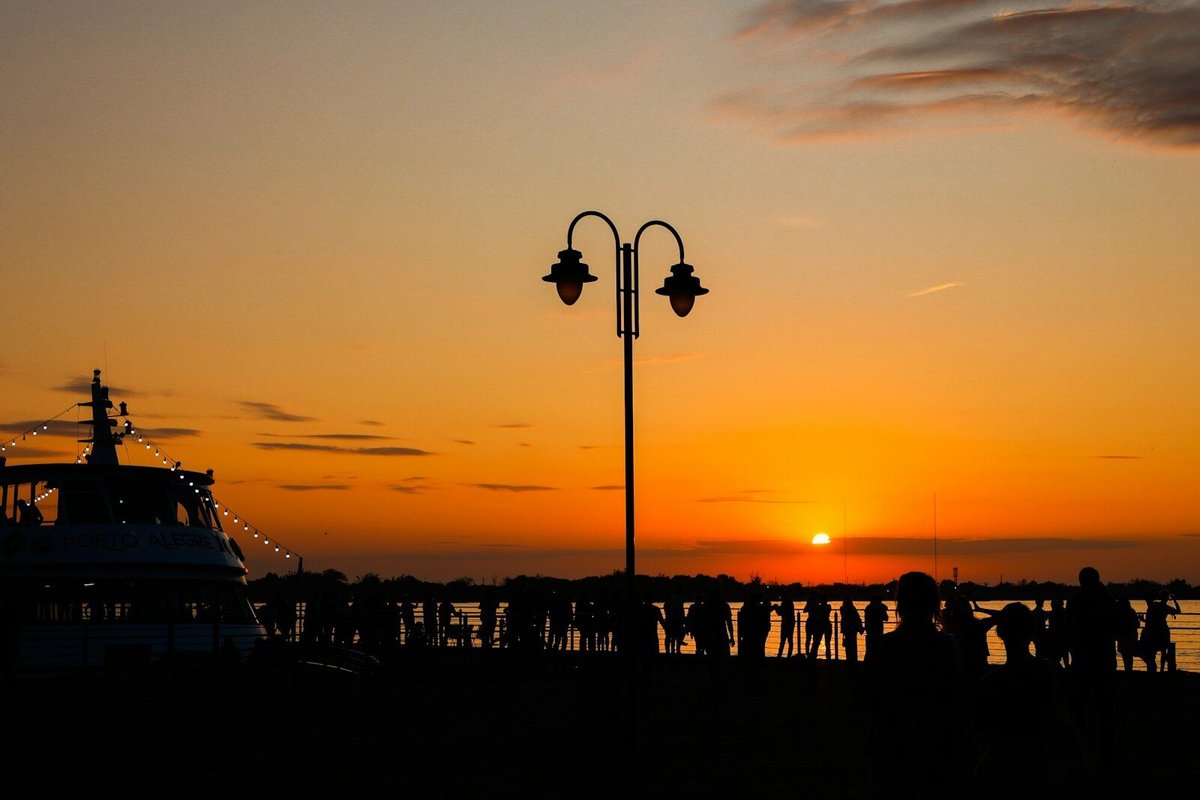 um grupo de pessoas em pé ao lado de um barco ao pôr do sol