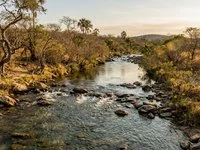 Rio de águas claras com pequenas corredeiras e pedras, cercado de vegetação de cerrado ao fim da tarde