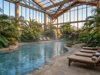 Piscina de águas termais com vapor leve ao amanhecer, cercada por palmeiras e espreguiçadeiras vazias