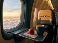 Janela de avião ao pôr do sol com nuvens douradas e uma pequena bola de Natal vermelha no peitoril